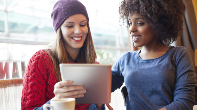 Two friends having a coffee while looking at the tablet smiling