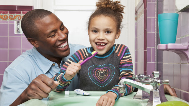 Father teaching his daughter how to brush her teeth