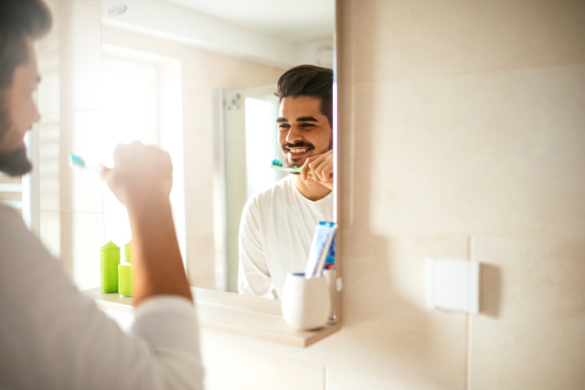 man brushing his teeth with Colgate toothbrush in front of mirror